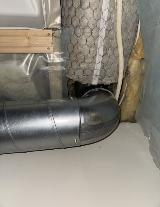 Ventilationsrör i metall med 90-graders böj installerad i taket, omgiven av isolering och en träram, i samband med köksfläktinstallation.