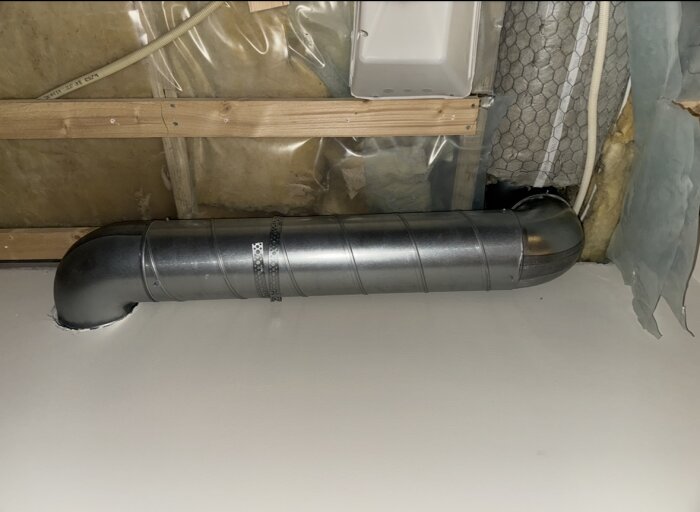 Ventilationsrör med två 90-graders böjar installerat under takbjälkar i en renoverad hall.