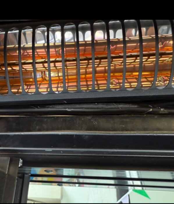 Bränd eller smält kabel inuti en värmare med metallgaller, visas för bedömning av skada och potentiell påverkan på elsystem.