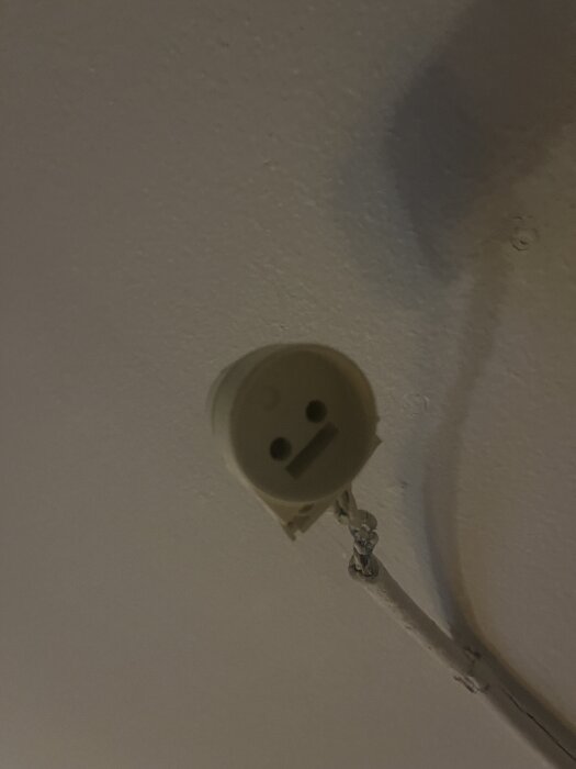 Takmonterat lamputtag i en äldre lägenhet med synliga kablar, som användaren undrar över kompatibilitet och stickpropp.