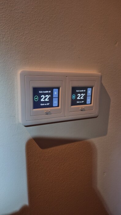 Två nya termostater från Plejd installerade i dubbelram på vägg, visar inställd temperatur på 22 grader för olika zoner.
