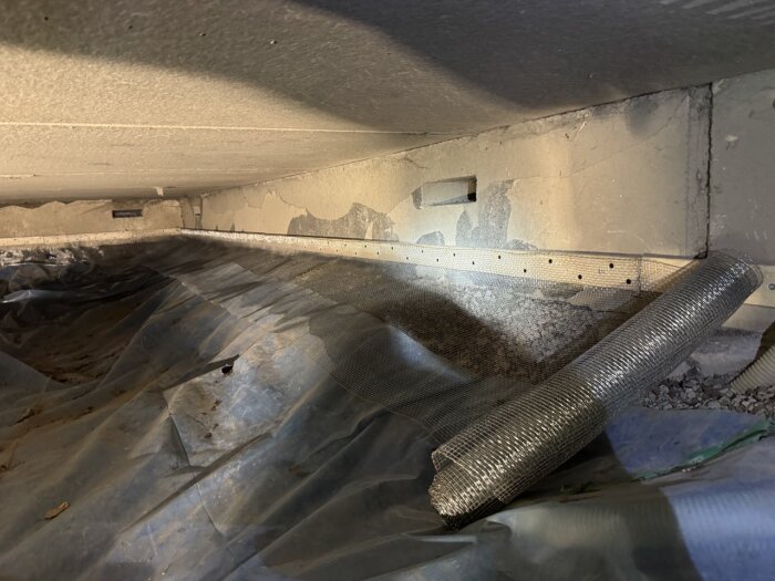 Galvaniserad järntrådduk rullad och installerad längs grunden i en krypgrund, med plastskikt på marken för fuktisolering.