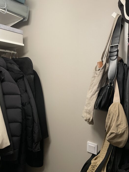 Klädhängare i skrubb med jackor och väskor på krokar. Nyligen spacklad och målad vägg syns i bakgrunden.