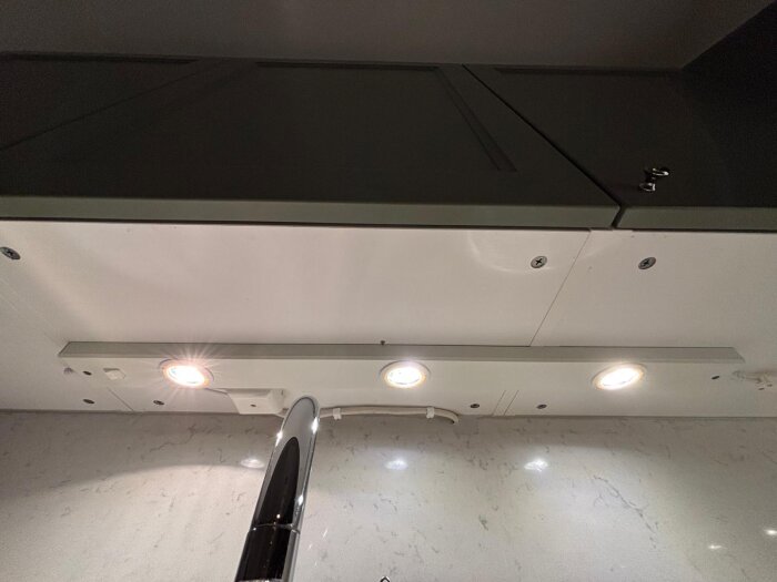 Armatur med tre spotlights ovanför diskbänken, med synlig fyrkantig dosa och inbyggd belysning under skåp.