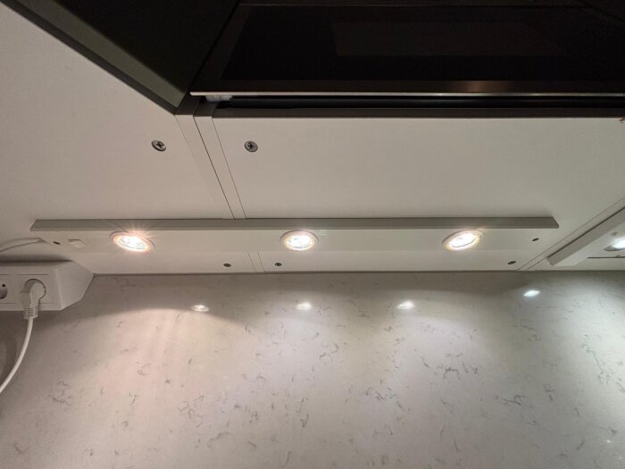 Tre takmonterade lampor ovanför diskbänk i kök, två tända.