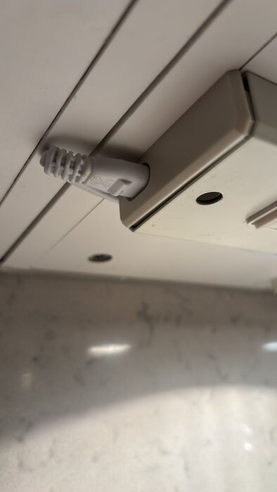 Vit fyrkantig elektrisk dosa monterad i taket ovanför diskbänken med en ansluten elkabel.
