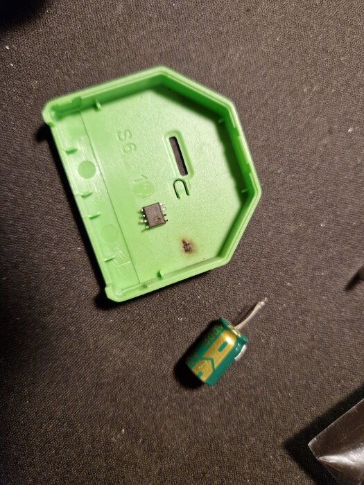 Grön plastdel och elektronisk komponent på mörkt underlag efter reparation av Dimmer2.