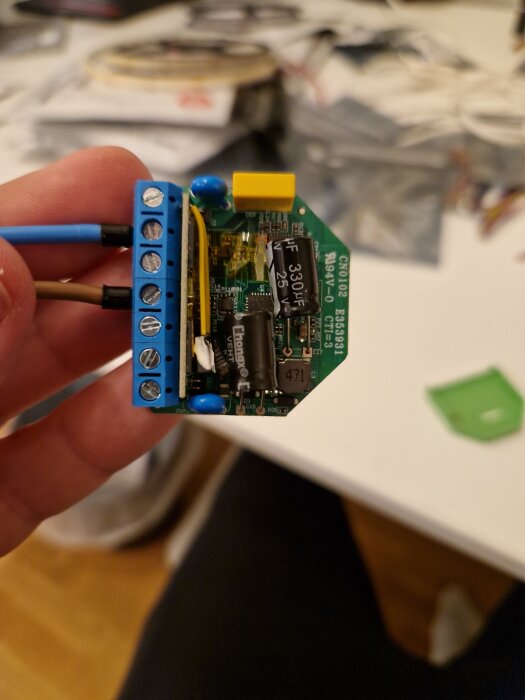 Elektronisk komponent av en Dimmer2 hålls i handen, med blå kopplingsplint och synliga kondensatorer.