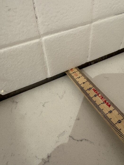 Mätskala som visar glipa under kaklad vägg och stenskiva i köket.