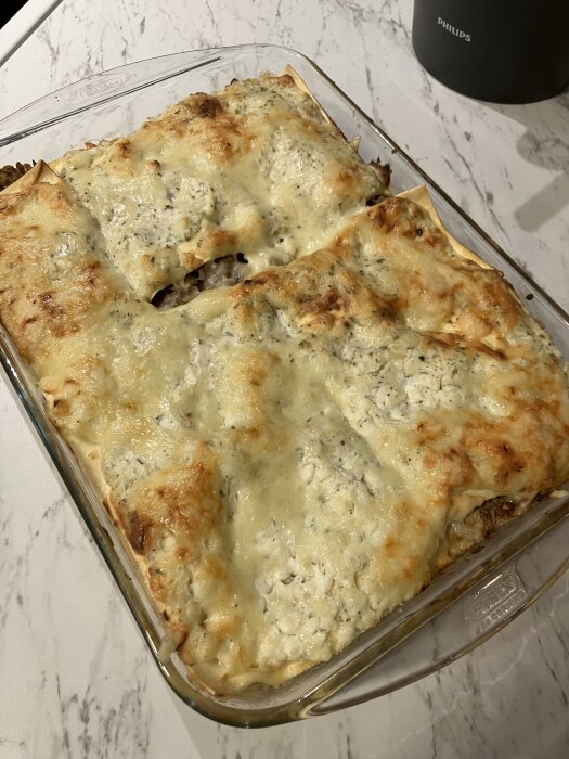 Lasagne tillagad utan bechamelsås, med ricotta, riven ost samt grädde eller mjölk i en glasform på marmorbord.