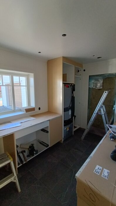 Köksrenovering med pågående installation av skåp och apparater, stege och verktyg synliga.