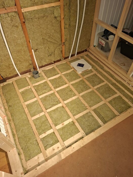 Golvisolering utan luftgap i ett badrum under renovering i en trästuga med synliga träbjälkar och isoleringsmaterial.