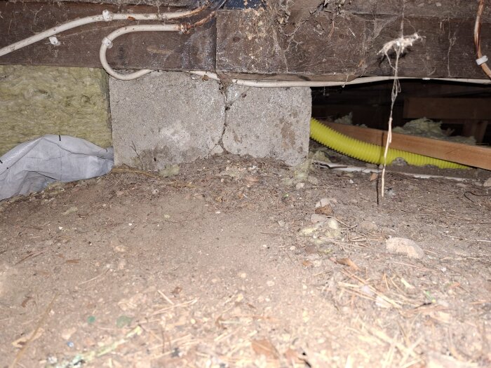 Krypgrund under en trästuga med isolering utan luftgap mot marken, synliga kablar och rör, samt placering av byggmaterial och isolering.