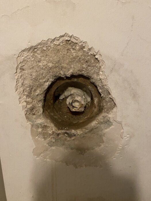 Gammalt rör med vattenledning i en putsad vägg, delvis fylld med fogskum; tecken på fukt runt rörets kant i källaren på ett äldre hus.