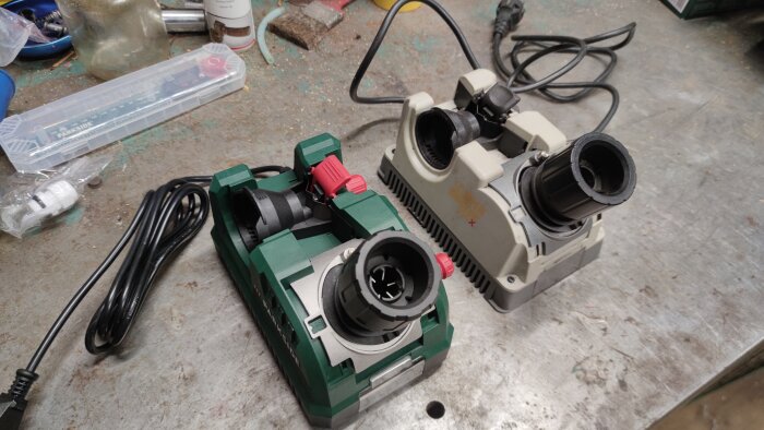 Två bänkslipmaskiner för borstar, en grön Parkside och en grå DrillDoctor, placerade på ett arbetsbord med sladdar.