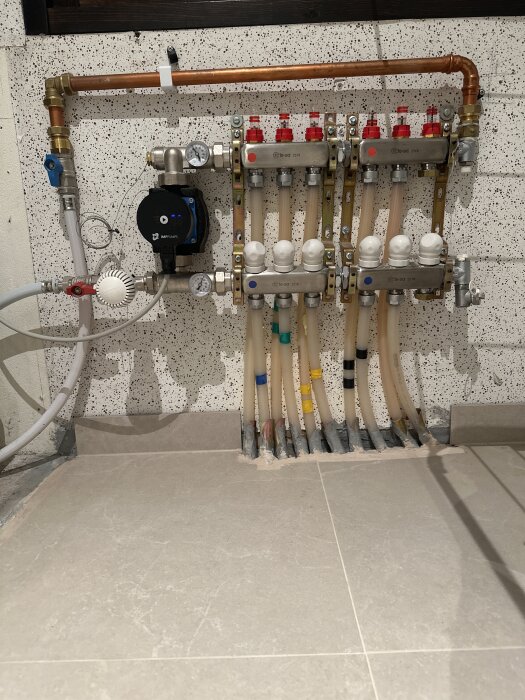 Golvvärmesystem med IMI Pumps NMT Mini monterad upp-och-ner, med flera anslutna rör och kopplingar på en vägg.