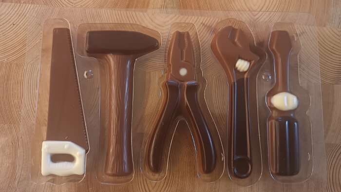 Chokladverktyg i plastförpackning, inklusive såg, hammare, tång, skiftnyckel och skruvmejsel, på träbord.