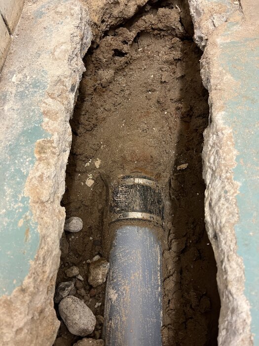Avloppsrör i källare med skarv vid gjutjärnsrör, omgiven av grus och synlig betongkanten.