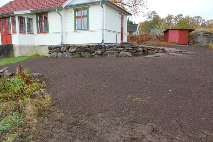 Nyplenad gräsmatta framför ett vitmålat hus med rött tak och stengrund.