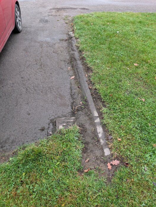 Asfaltväg med tydlig kant mot gräsmatta, där gräset verkar nyklippt eller nyligen bearbetat, grus utspritt på vägen.