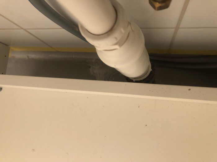 Rör och vit bänkskiva i badrum, del av renoveringsprojekt där vask ersatts. Diskussion om avstängningsventilens placering över eller under bänk.