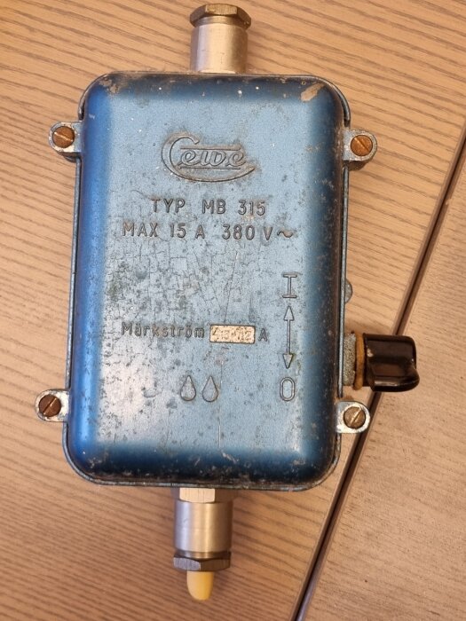 Blå elektrisk apparat med texten "Cewe TYP MB 315 MAX 15 A 380 V" och märkström 4,5-7,2 A, mot träbakgrund.