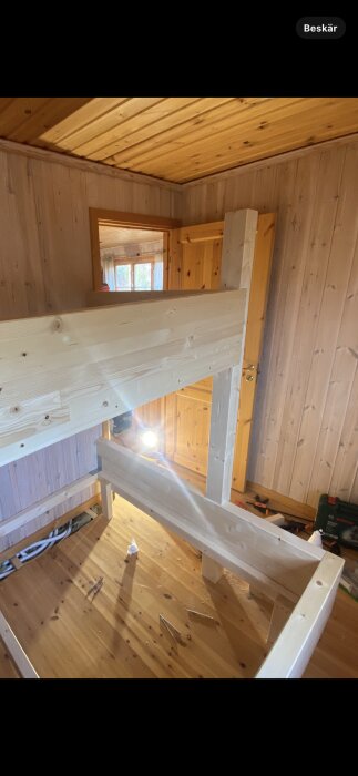 Trätak och väggar i en stuga med en delvis färdigmonterad trästruktur och verktyg på golvet.