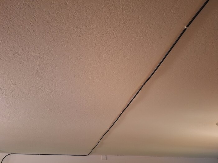 Svart HDMI-kabel klamrad i taket, sträcker sig längs en vit vägg.