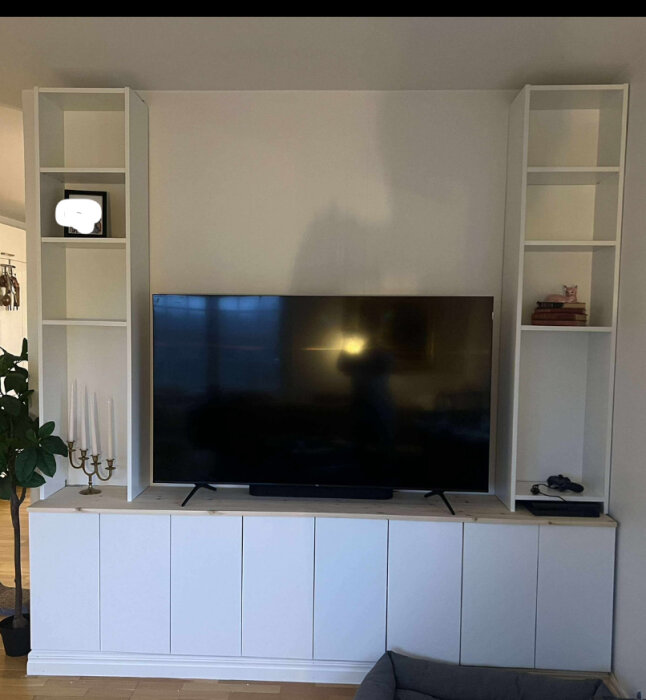 Platsbyggd tv-möbel med vita IKEA-stommar, hyllor på sidorna och utrymme för en stor TV. Kandelaber och prydnad på vänstra hyllan.