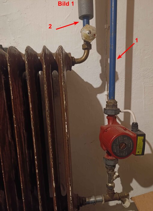 Cirkulationspumpen är kopplad till ett element med två rör. Ett blått rör går in i pumpen, som är monterad på väggen.