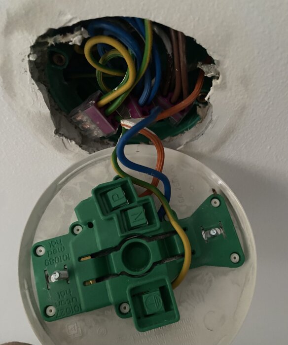 Elinstallation med taklampa; synliga kablar i olika färger inklusive orange, anslutna till grön hållare märkt N, P, och jord.