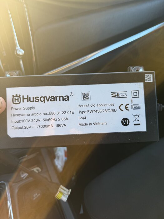 Husqvarna strömförsörjningsenhet i en bil med specifikationer på en etikett, inklusive artikelnummer och tillverkningsland.
