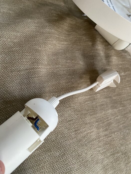 Vit stickpropp utan jordning med synliga kablar ligger på en brun matta.