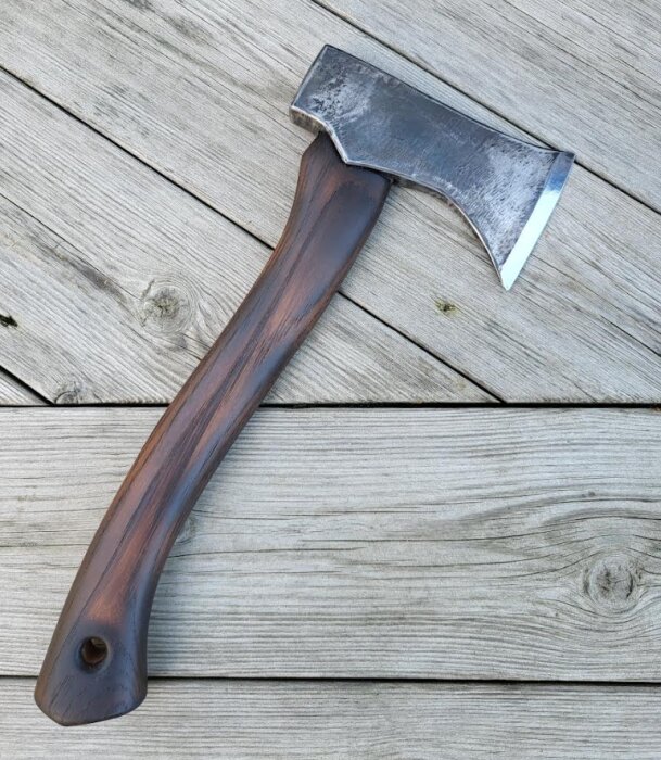 Yxa med mörkt trähandtag placerad på ljusa träplankor.