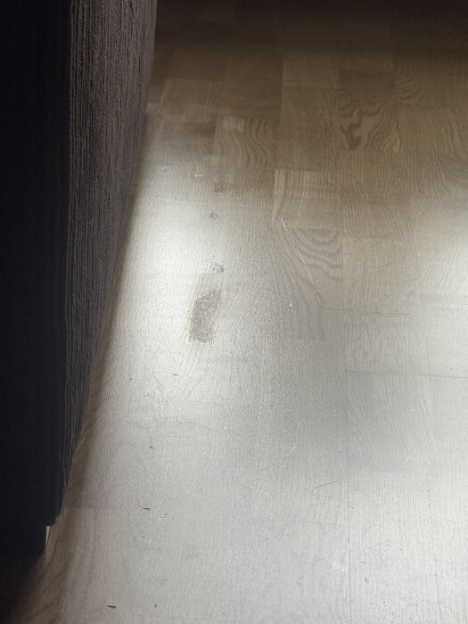 Parkettgolv med små blanka fläckar synliga vid släpljus, troligen orsakade av bortdragen lack efter tejpanvändning.