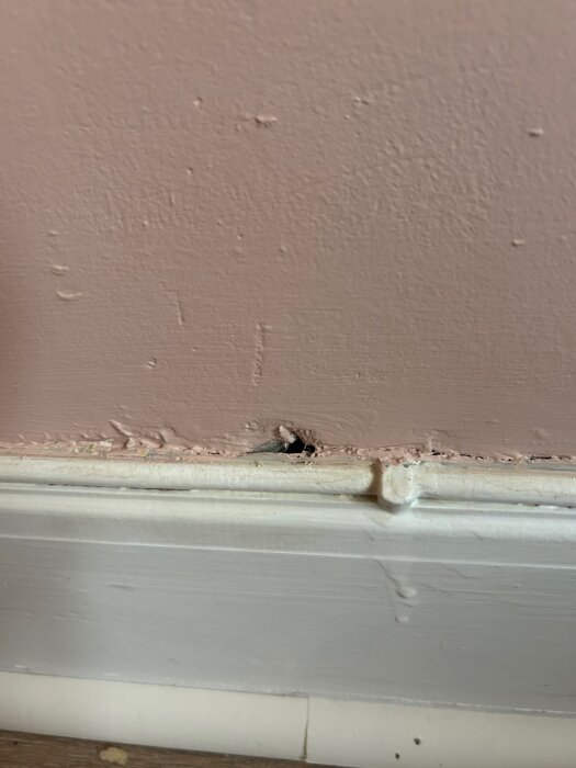 Hål i väggen ovanför golvlisten, visar ett mellanrum som orsakar drag. Rummet behöver tätas för att förbättra isoleringen.