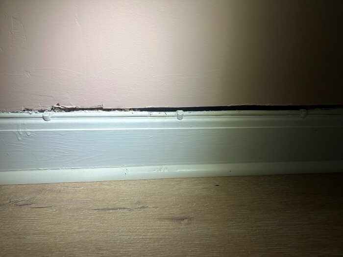 Sprickor mellan golvlist och vägg med drag, ofyllt hål på ett rum där åtgärder för isolering och tätning övervägs, synlig strukturskada.