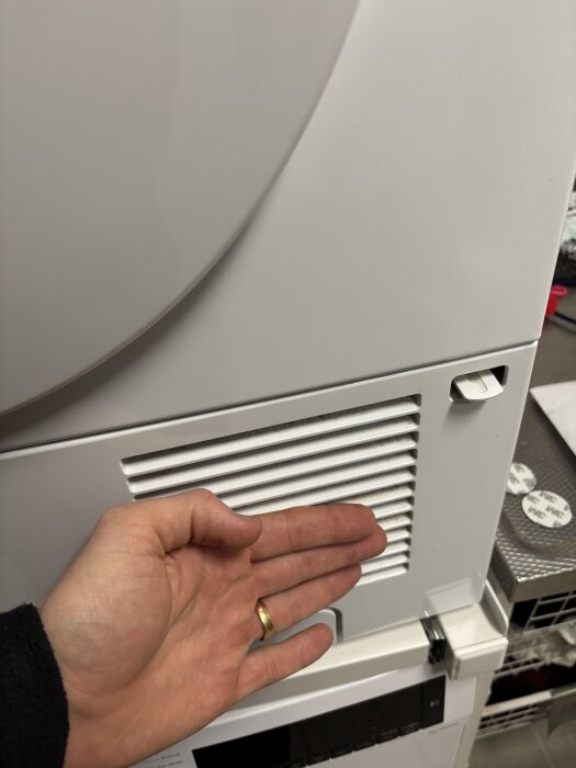 En hand placeras framför en vit ventil på en hushållsmaskin, förmodligen för att känna luftflödet.