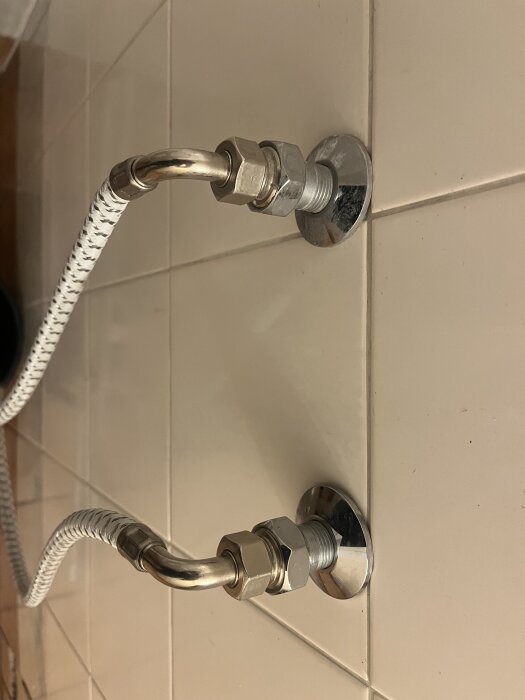 Duschanslutningar med rör och fasta muttrar på vit kakelvägg, redo för installation av en duschblandare, visar 160cc avstånd mellan fästen.