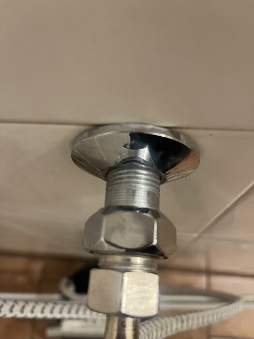 Metallmutter och röranslutning monterad mot en väggplatta, synlig del av VVS-installation bakom en avlägsnad duschkabin.
