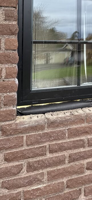 Mexitegelvägg med svarta fönsterramar; fogarna mellan tegelstenarna verkar delvis sakna murbruk.