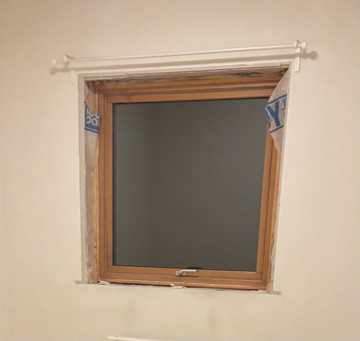 Fönster med träkarmar och exponerat vindskydd i en renoveringssituation, omringat av gipsskivor.