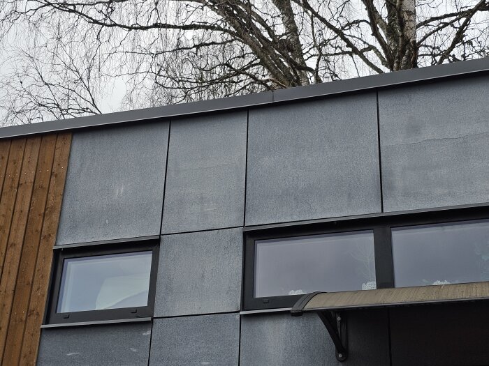 Attefallshus med sprickor i fasaden och fönster under en grå dag.