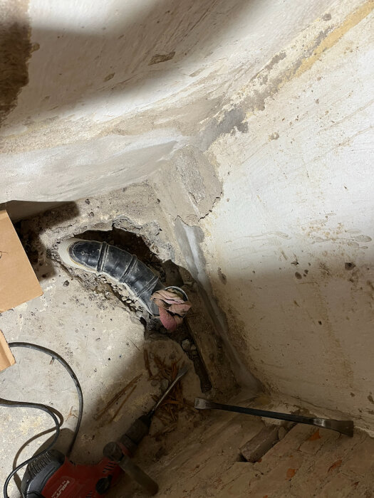 Uppbilat golv i källare med synligt avloppsrör och verktyg, för förberedelse av installation av ny vägghängd toalett.