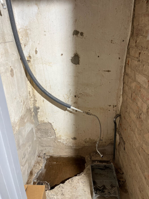 Vägg i källare med öppet golv där rör förbereds för ny avloppsinstallation. Hyllade verktyg och material syns i bilden.