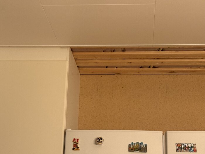 Taköppning i kök efter demontering av luckor visar ouppfört tak bakom kylskåp, med träbalkar synliga.