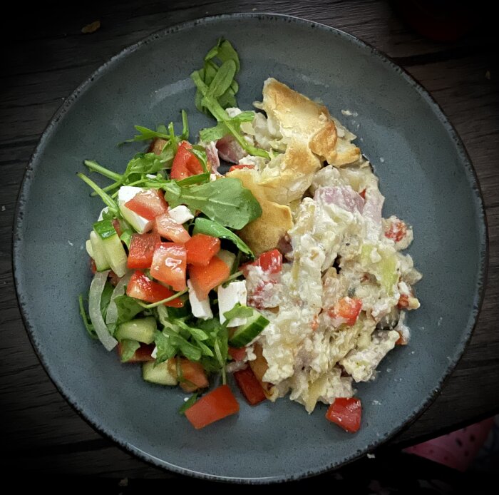 Paj med vitkål, skinka, kyckling, paprika, mögelost och ost täckt i ett pajskal, serverad med en färgglad fetaostsallad på tallrik.