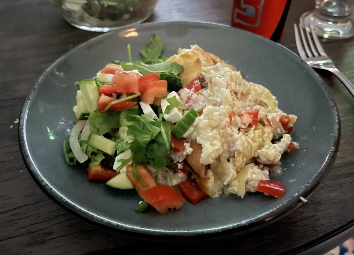 Paj med vitkål, skinka, kyckling, paprika och ost serverad med en sallad av tomat, gurka och fetaost på en tallrik.