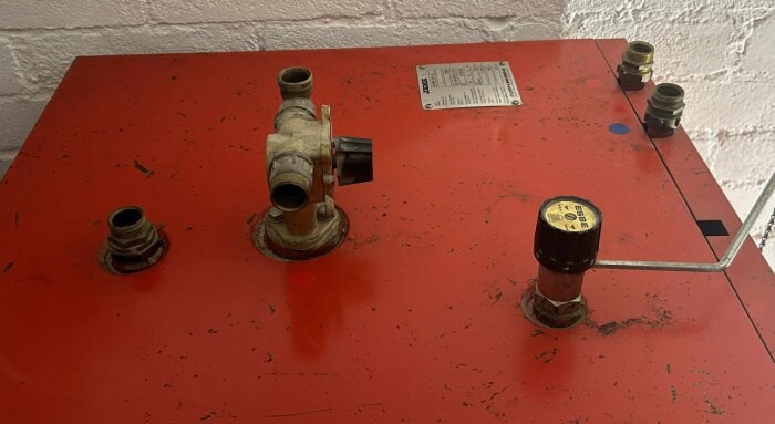 Ovansidan av en kombipanna med röranslutningar märkta med blå och röd etikett, samt en blandningsventil i mitten och ett okänt rör till vänster.