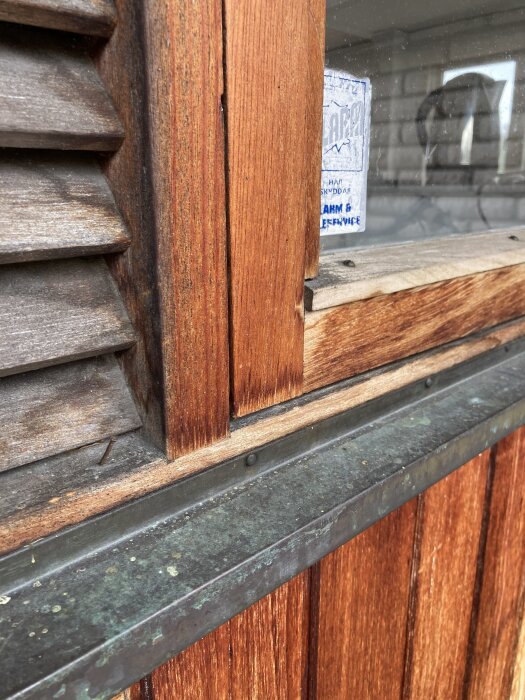 Närbild av ett 60-talsfönster med träram och luftningslucka, synligt kopparbleck och etikett på glaset.